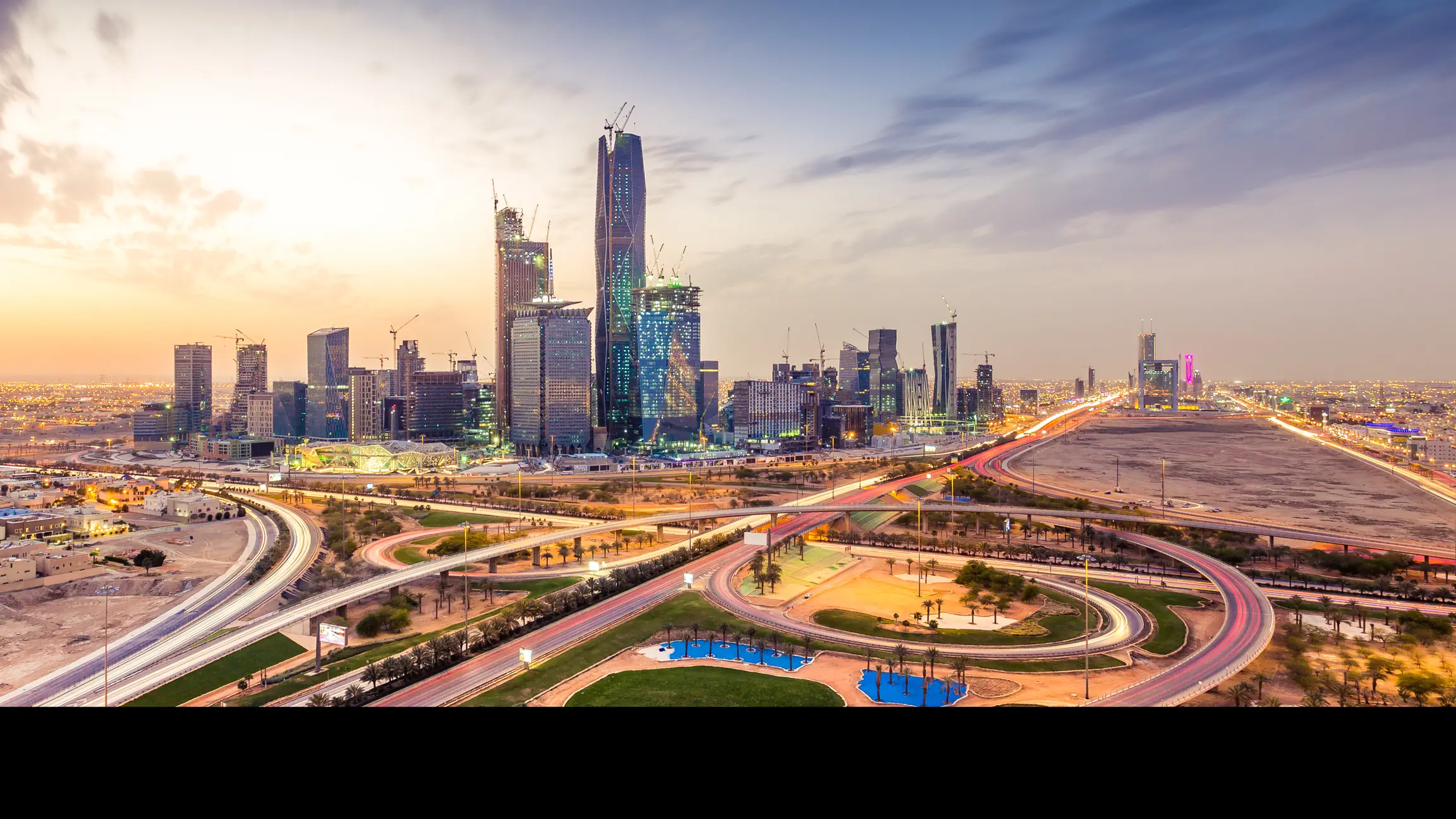 Riyadh at sunset from the air — the towers of King Abdullah Financial District above the lit interchanges of the Olaya corridor